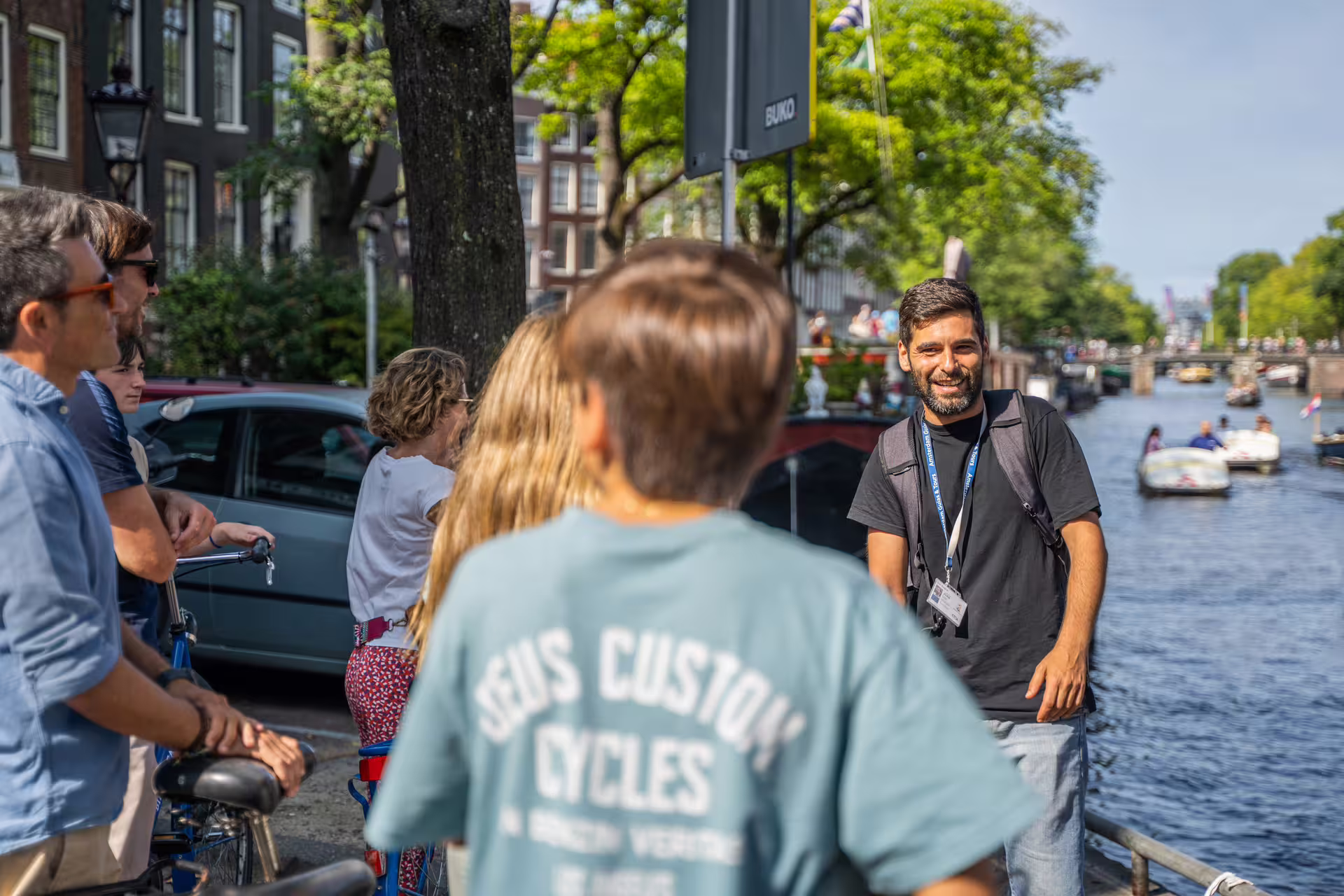 Group enjoying a sunny Amsterdam bike tour with guide, overlooking scenic canal boats, perfect for a canal cruise experience.