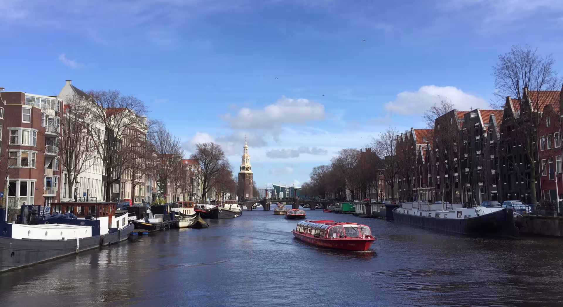 Scenic view of Amsterdam canal with historic buildings and a red boat, perfect for a bike tour and canal cruise experience.