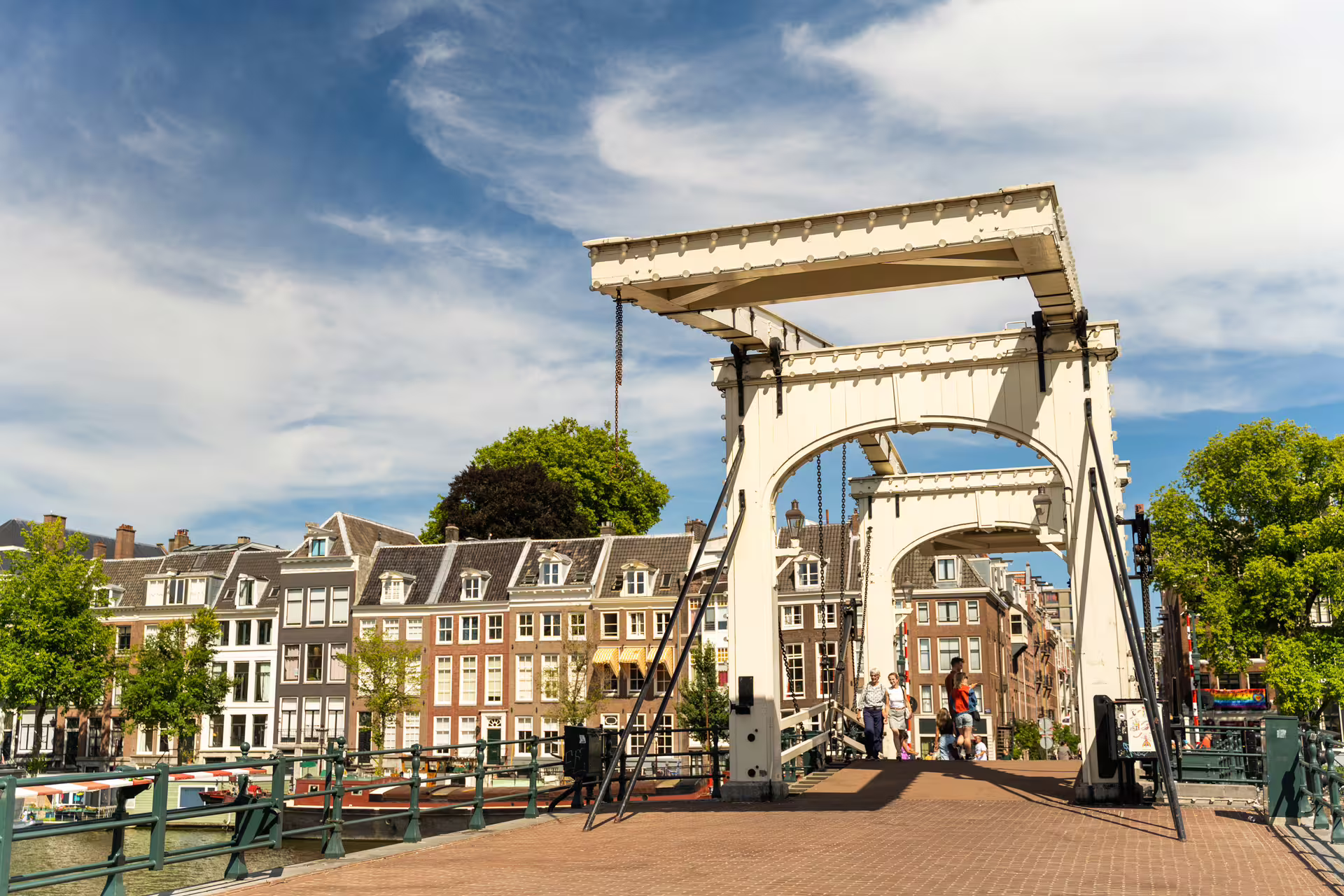 Historic Amsterdam drawbridge over a canal with cyclists and pedestrians, showcasing traditional Dutch architecture and vibrant city life.