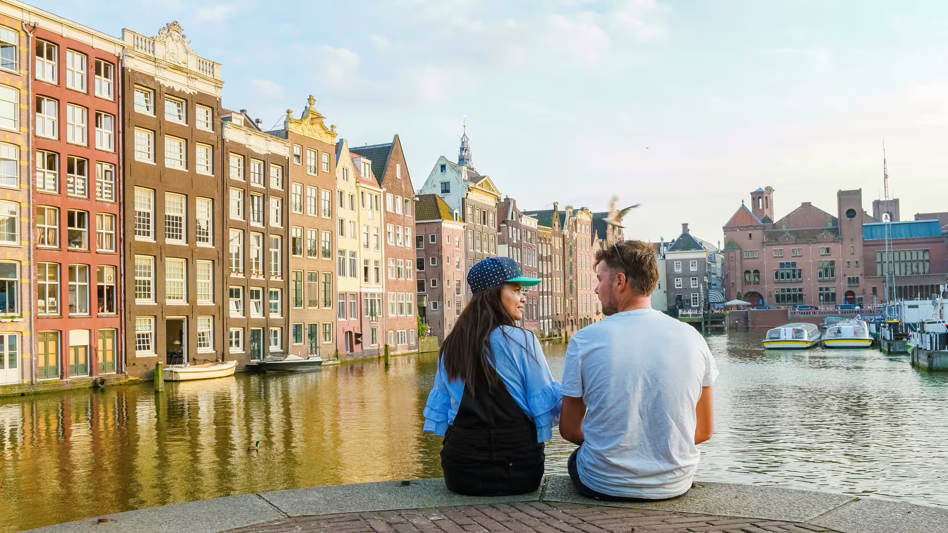 Couple by Amsterdam canal with historic canal houses, ideal 1-day walking tour with multilingual audioguide