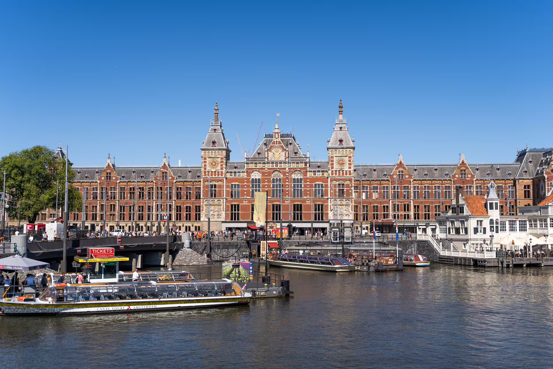 Amsterdam Centraal Station with canal tour boats, perfect for exploring the city's historic architecture and waterways by bike.