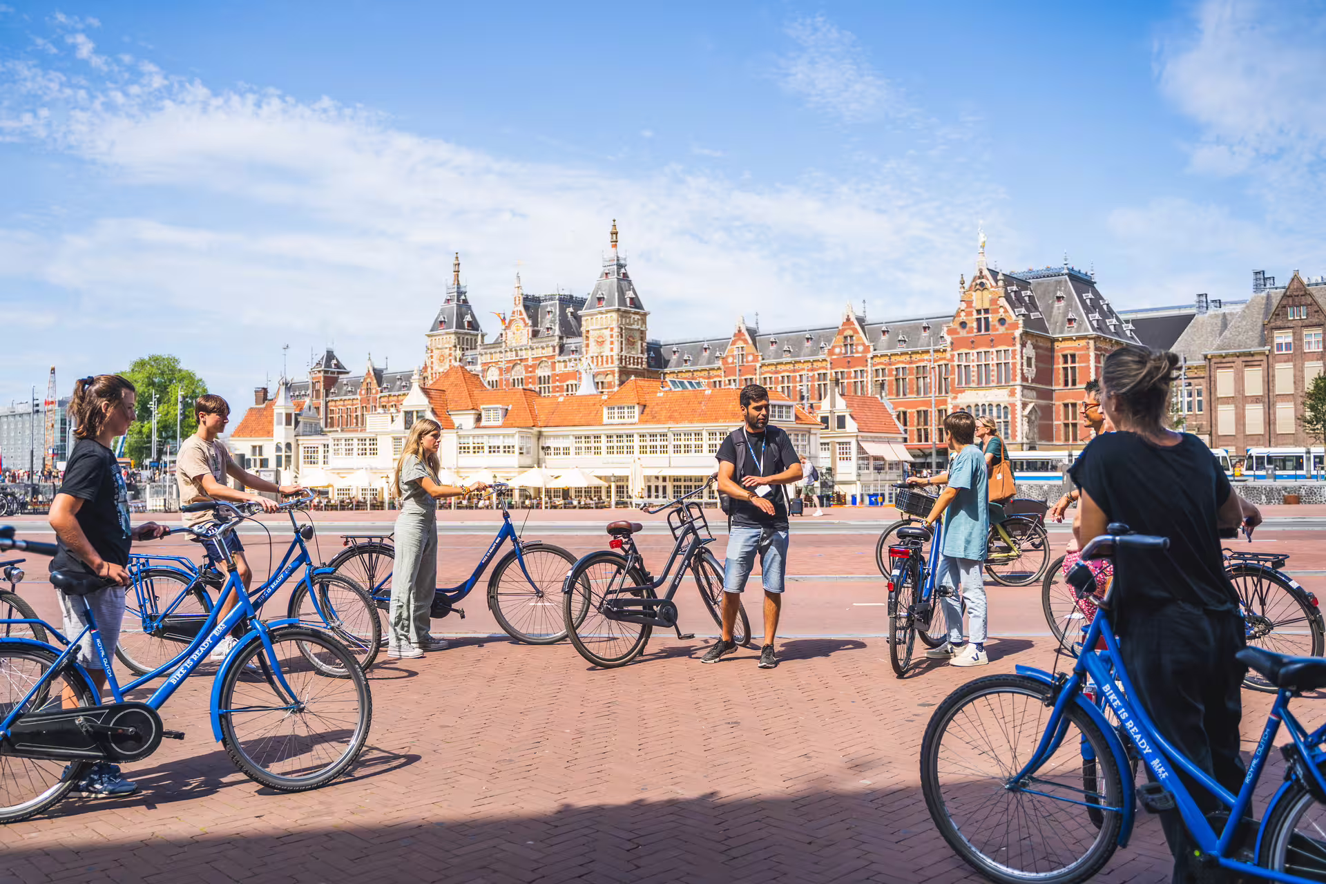 Cyclists gather with bikes for a guided countryside private bike tour, showcasing scenic architecture under a clear blue sky.