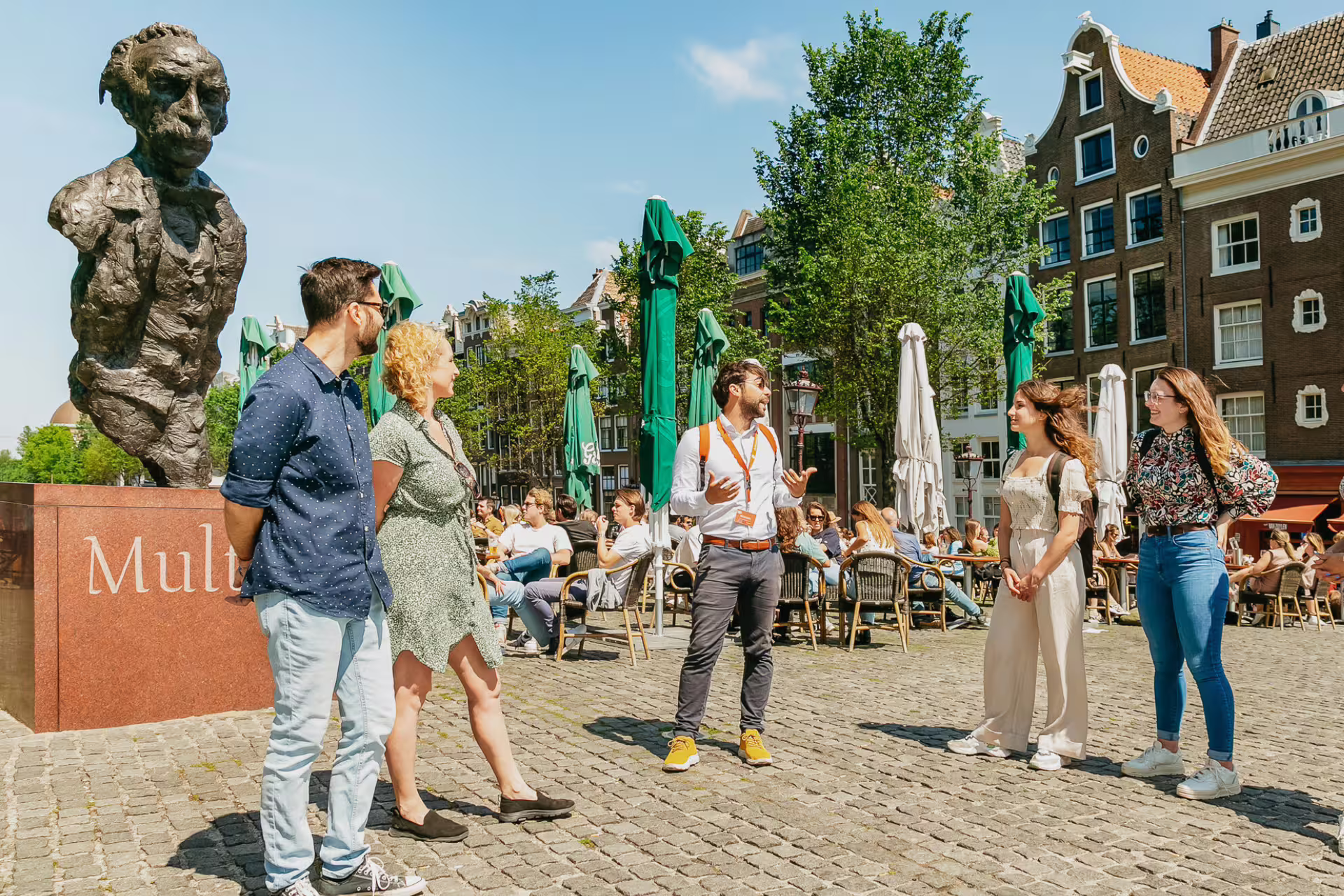 Tour guide leads a group past a historic statue in Amsterdam's lively square, uncovering hidden stories of the city.