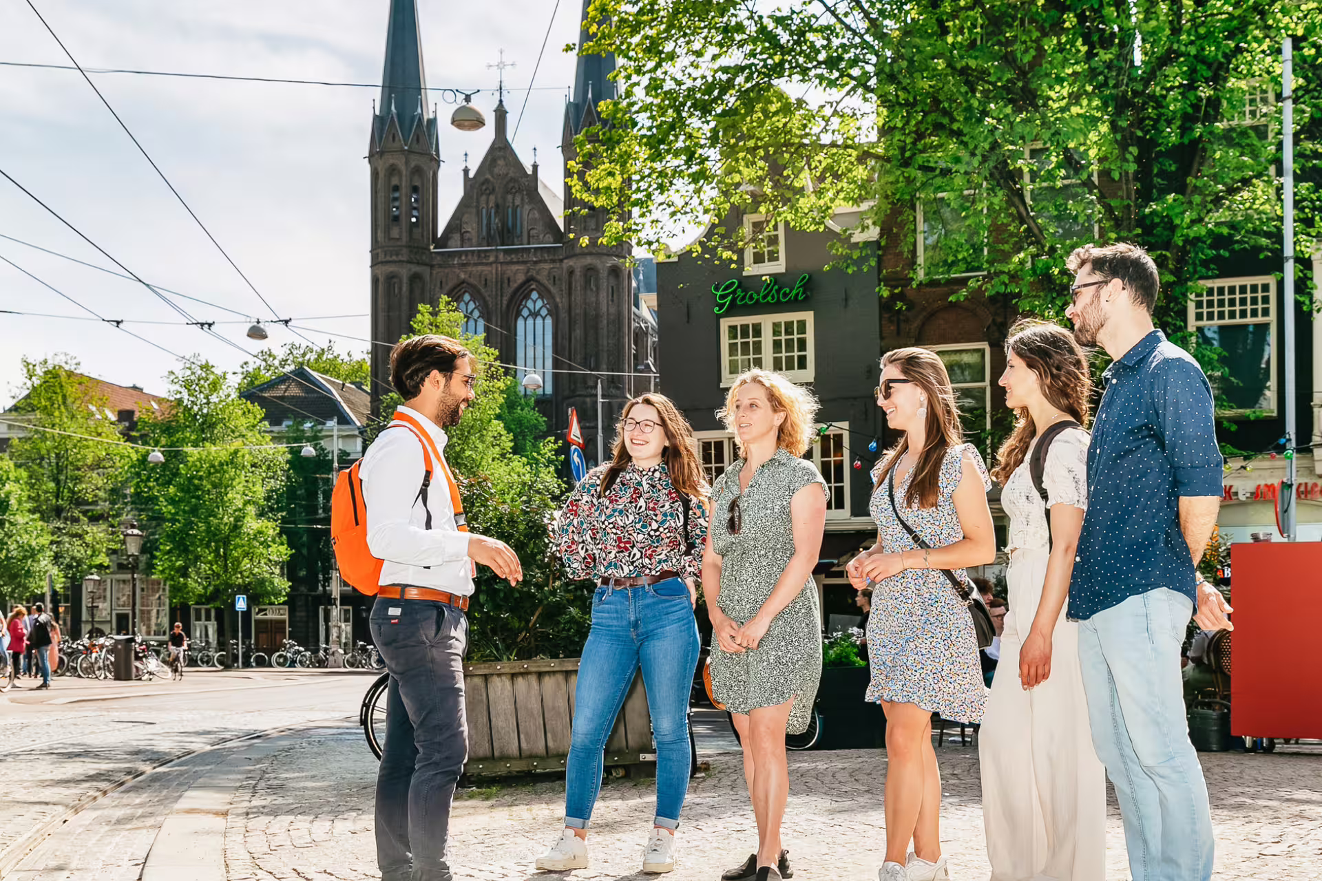 A guide leads a small group tour through historical Amsterdam, highlighting hidden secrets near iconic architecture on a sunny day.