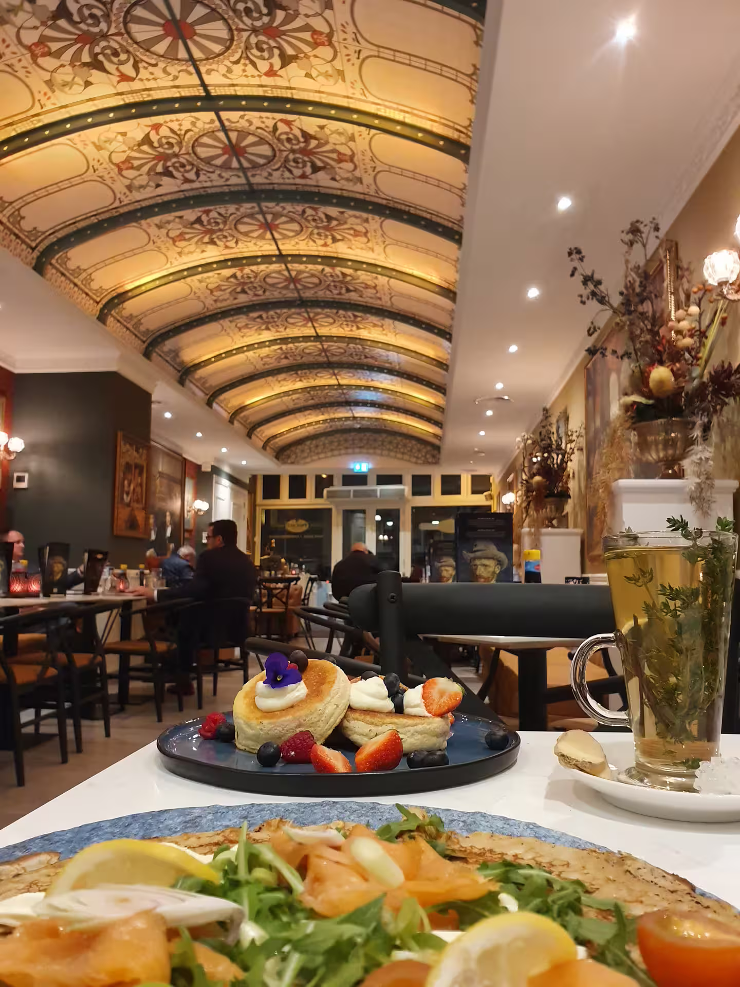 Cozy Amsterdam restaurant interior with ornate ceiling, featuring a table set with Dutch pancakes and herbal tea, perfect for a culinary tour.