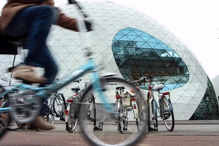 Cyclist passing modern Amsterdam landmark, ideal start for Amsterdam to Eindhoven private transfer via Schiphol