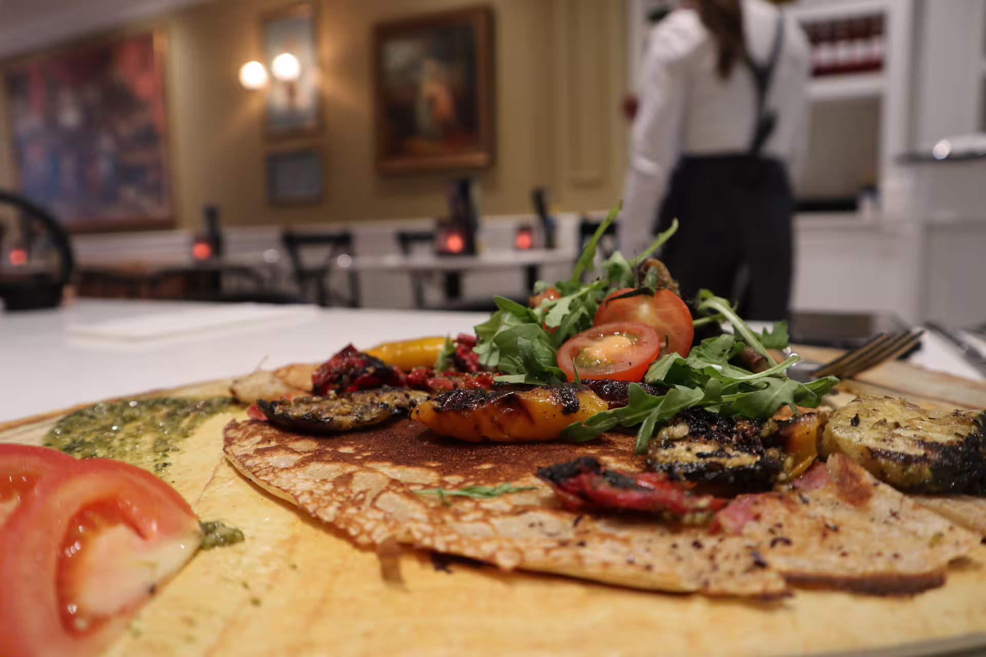 Delicious Dutch pancake topped with fresh arugula, tomatoes, and grilled vegetables in a cozy Amsterdam restaurant setting.