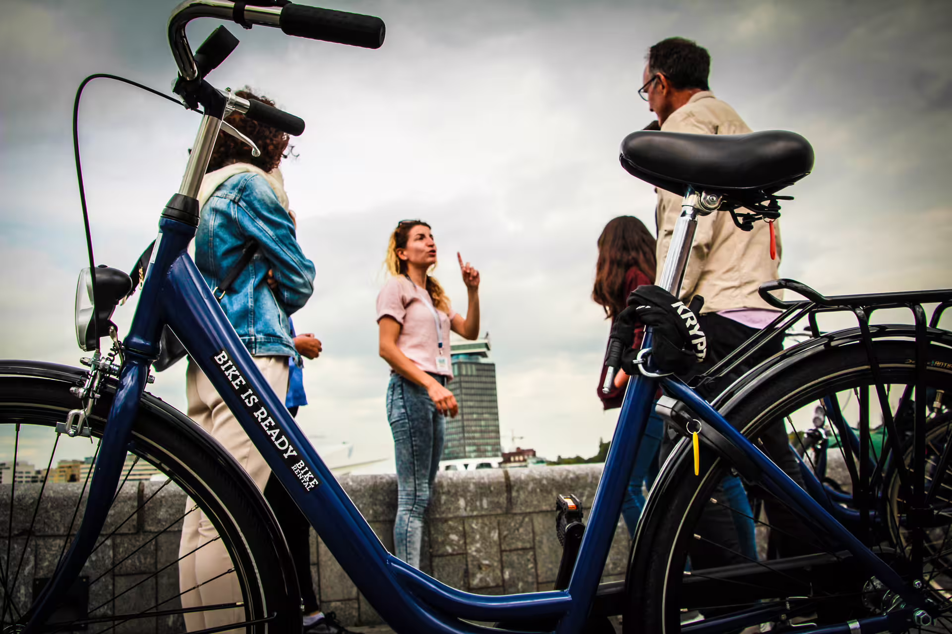 Tour group engages with a guide beside a parked bike in Amsterdam, showcasing city exploration and cultural experiences.