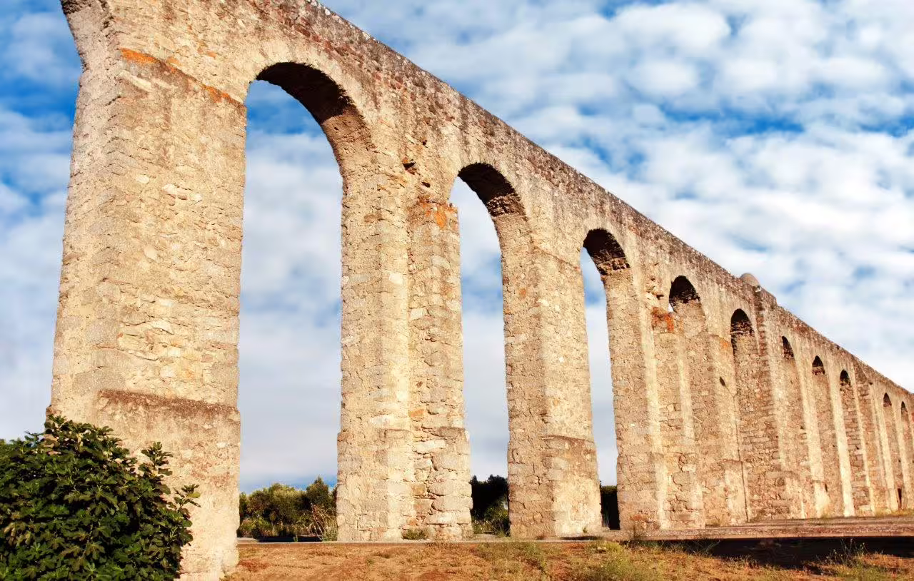 Ancient Roman aqueduct in Portugal under a blue sky, showcasing historical architecture on "The Best of Portugal" tour.