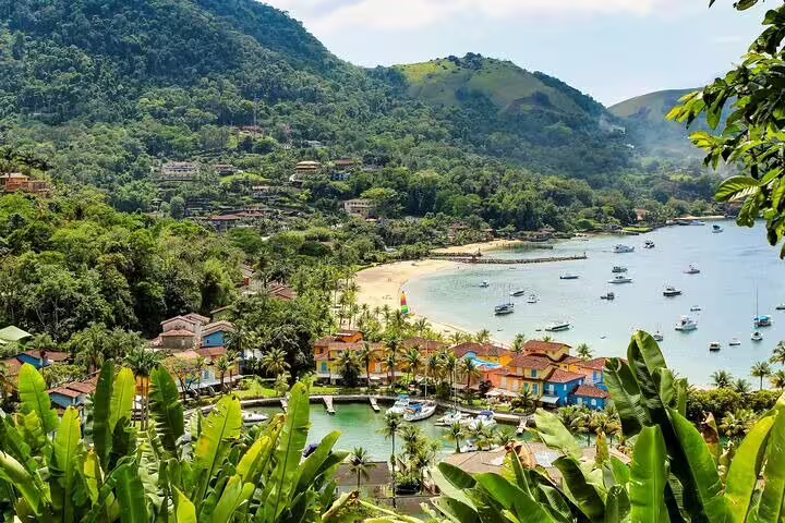 Aerial view of Angra dos Reis showcasing lush greenery, vibrant homes, and anchored boats for a speedboat tour.