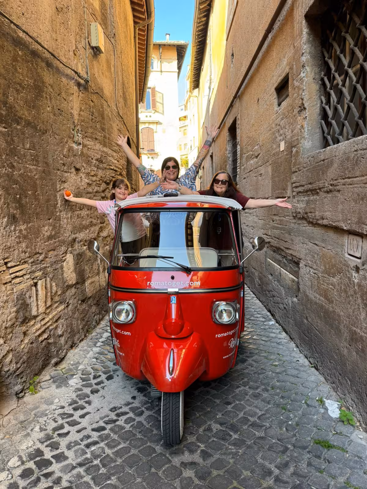 Tourists on an Ape Calessino navigating a narrow cobblestone alley during a lively early morning city tour.