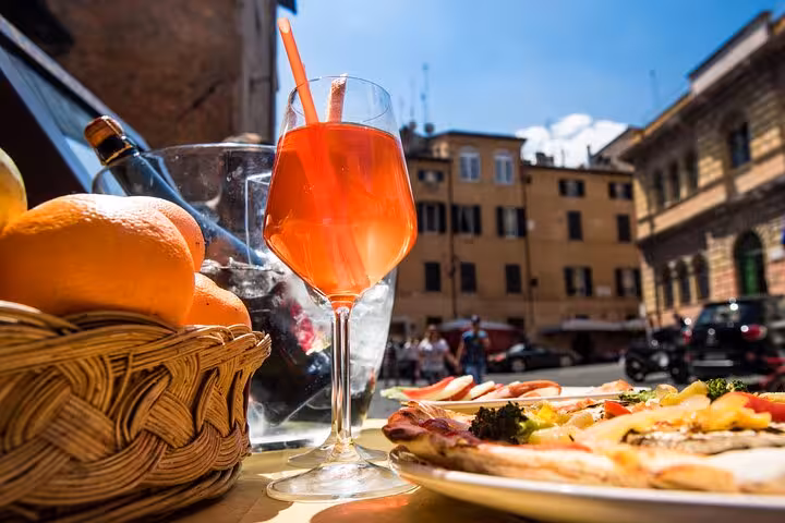 Refreshing Aperol Spritz with a basket of oranges and pizza in a sunny Italian piazza on the MaMa Florence Aperitivo Tour.