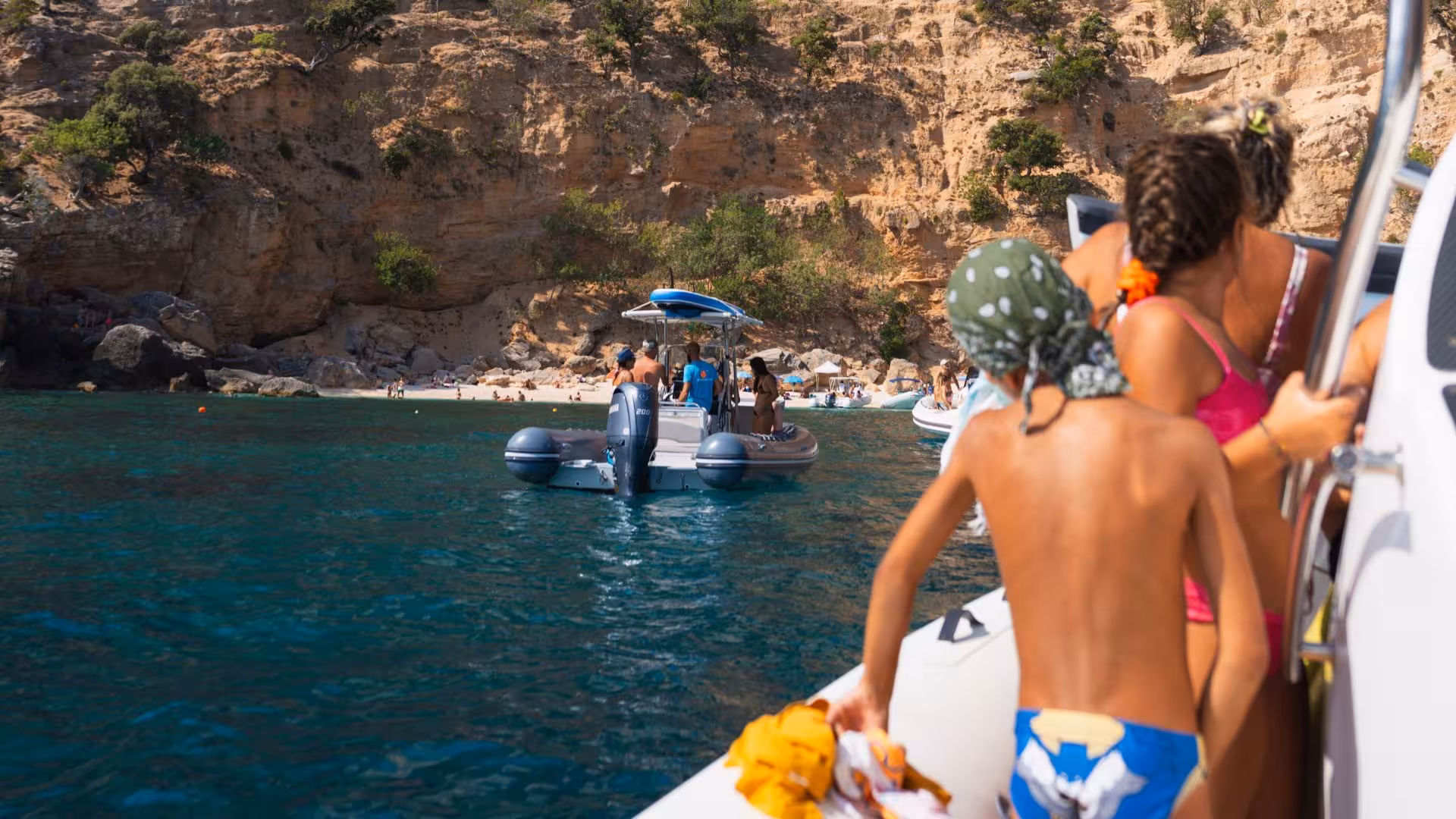 Family approaching Cala Mariolu's stunning beach by RIB boat, surrounded by clear blue waters.