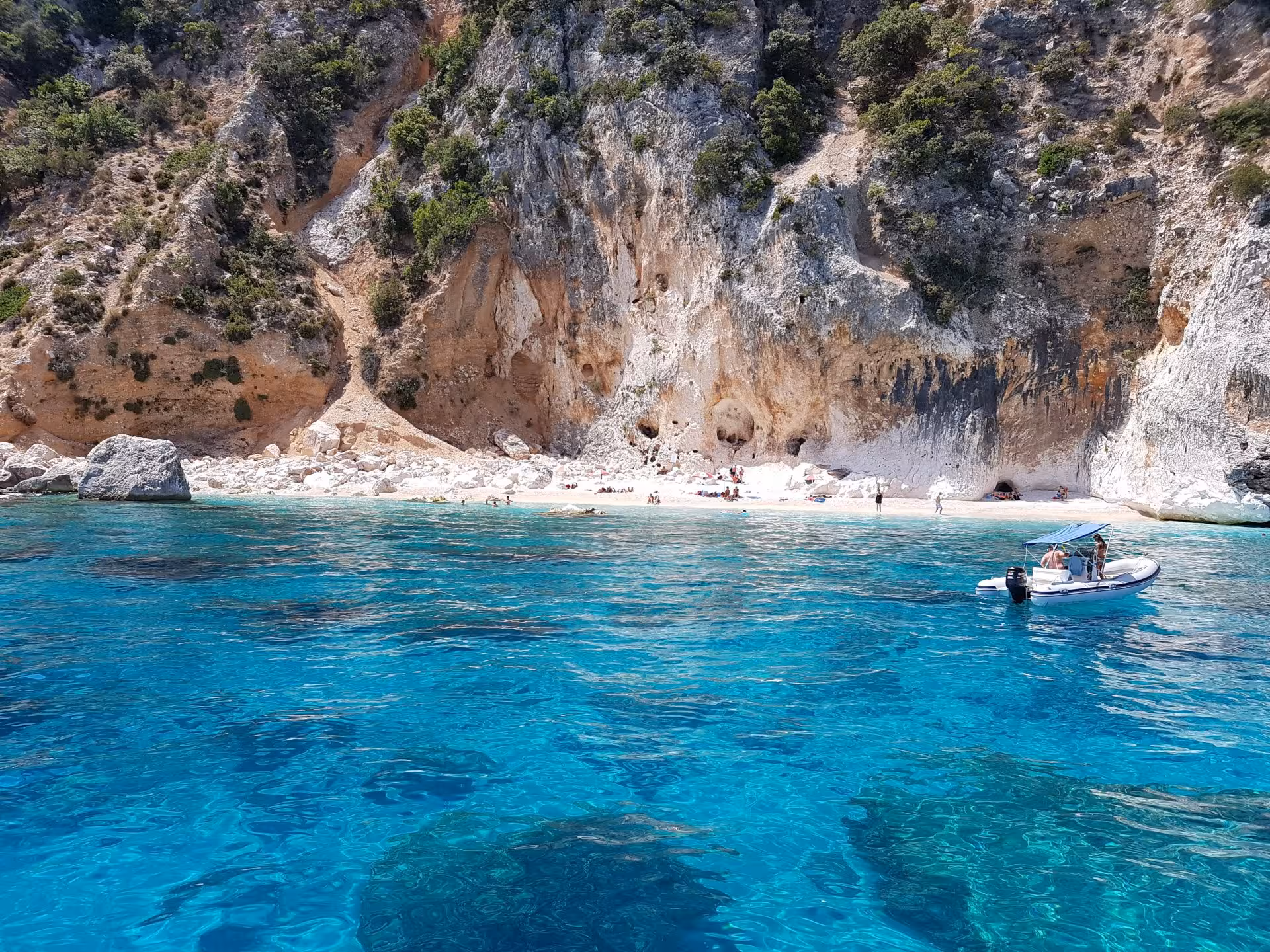 Visitors enjoying a secluded beach with turquoise waters and rocky cliffs during a sailing tour in the Gulf of Orosei.