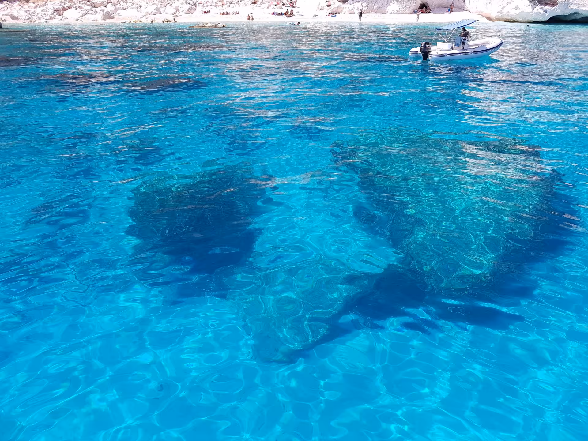 Pristine blue waters revealing submerged rocks near a boat, ideal for exploring the Gulf of Orosei from Arbatax.