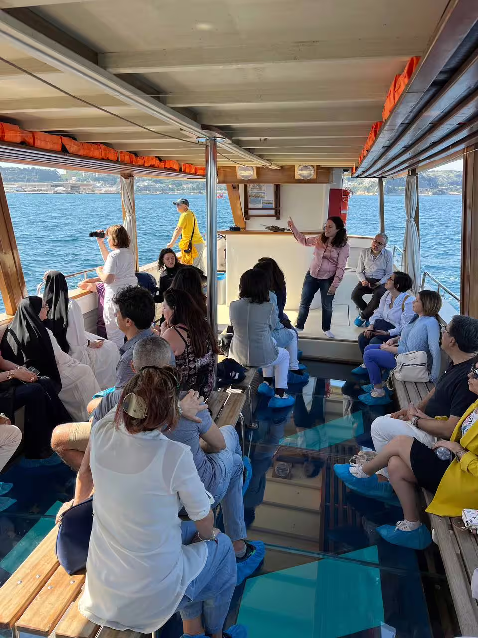 Guests listening to guide on Archeoemotions Baia Sommersa glass-bottom boat tour over underwater mosaics