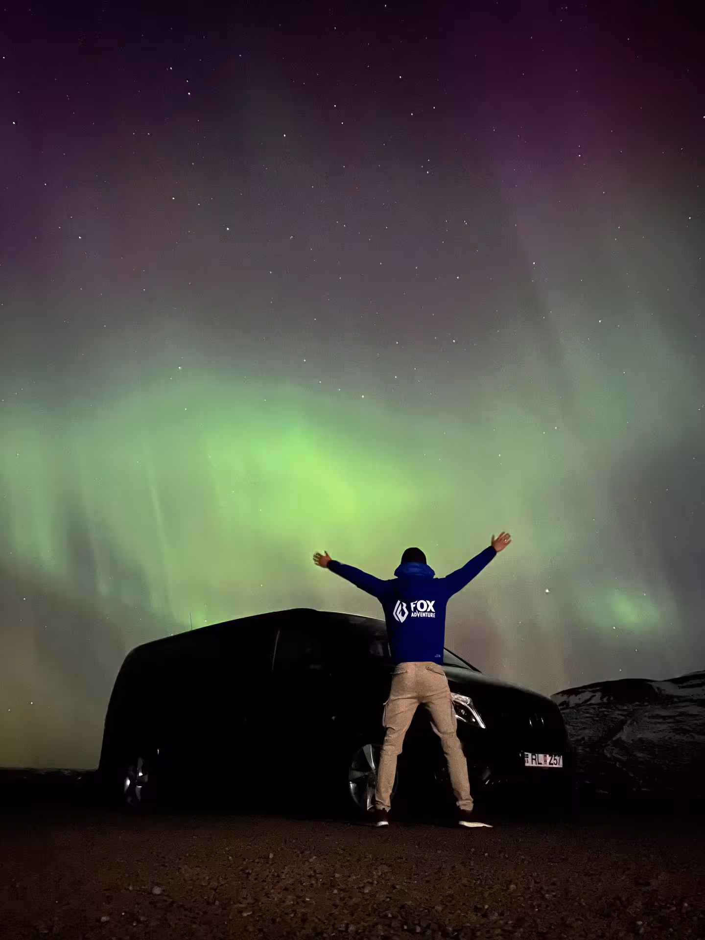 Traveler watching green Aurora Borealis beside a 4x4 at night, Arctic Odyssey northern lights tour moment