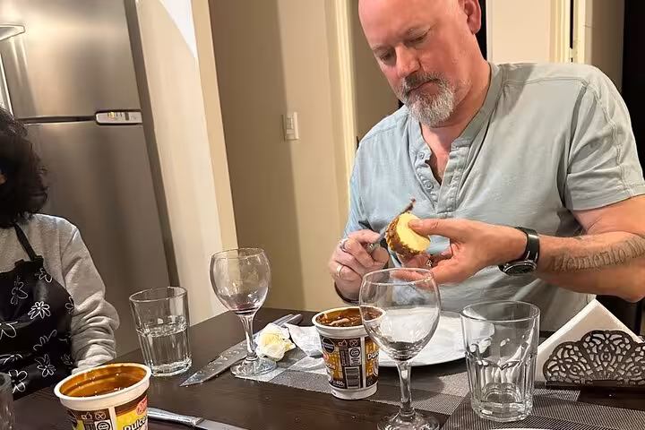 Participant savoring Argentinian dessert with dulce de leche, surrounded by wine glasses in a culinary class.
