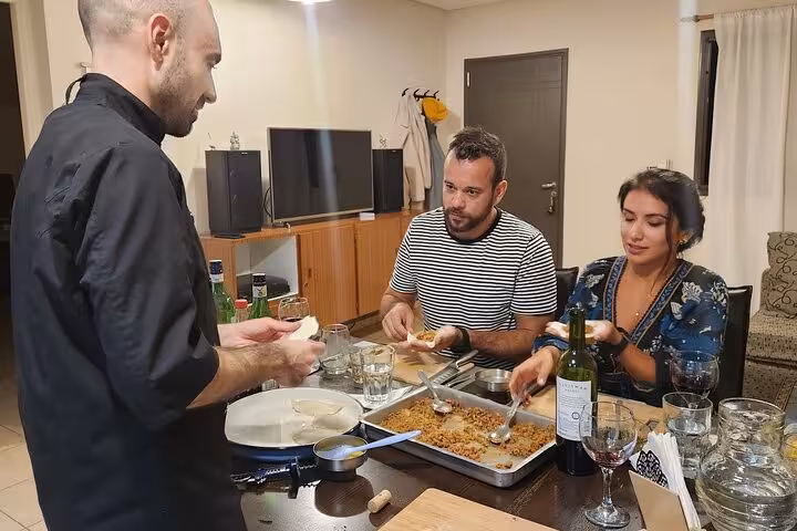 Guests enjoy preparing Argentinian dishes with a chef while sipping wine in a cozy kitchen setting.