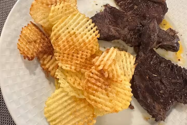 Argentinian dish with grilled steak and waffle-cut potato chips on a white plate for a culinary experience.