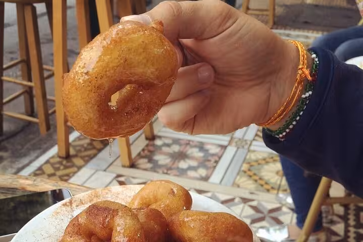 Hand holding loukoumades Greek honey donuts at a taverna, tasty stop on Athens by Night walking tour