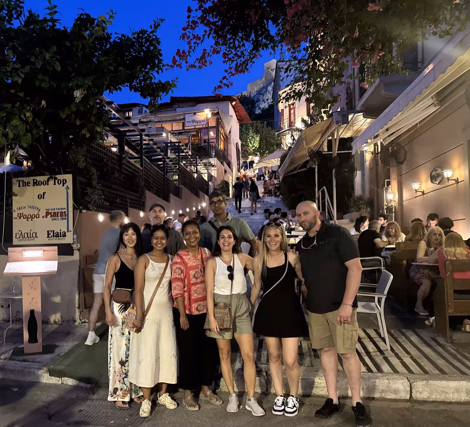 Group photo in Plaka on an Athens by Night walking tour, with lively tavernas and Acropolis views
