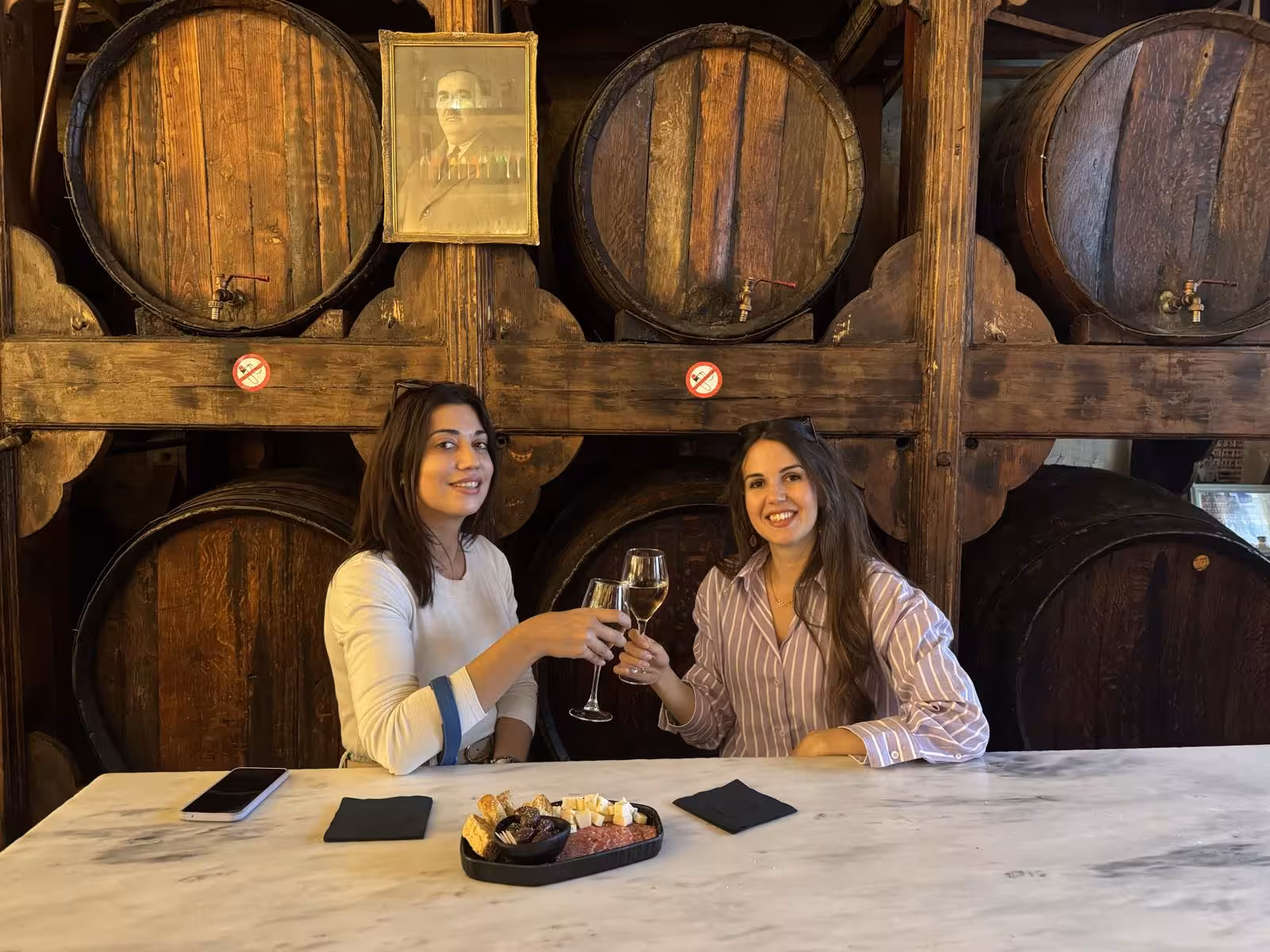 Friends toast Greek wine in a historic Athens wine bar with barrels, part of the Athens by Night tour