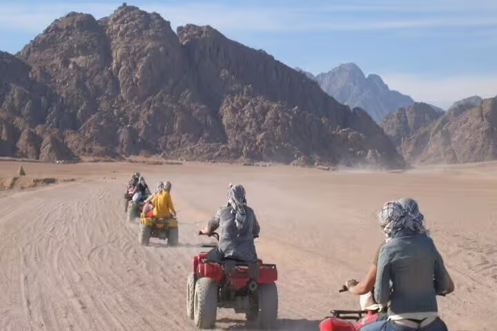 Riders on ATV quad bikes crossing Hurghada desert with mountain backdrop on safari adventure tour