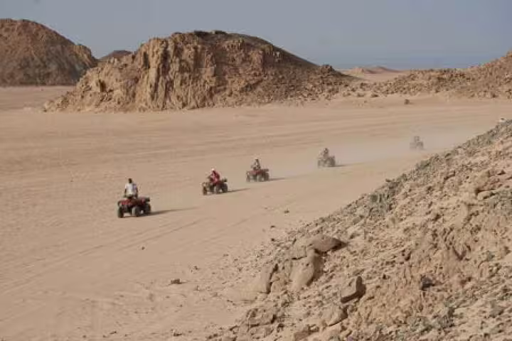 Group ATV quad bikes crossing wide Marsa Alam desert valley, Red Sea off-road safari before camel ride and dinner