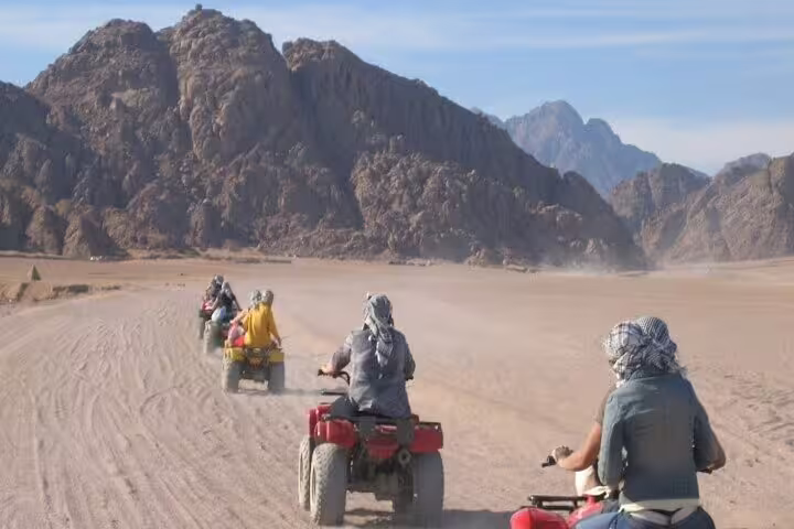 Riders on double ATV quad bike safari from Sharm El Sheikh crossing Sinai Desert valley with mountains