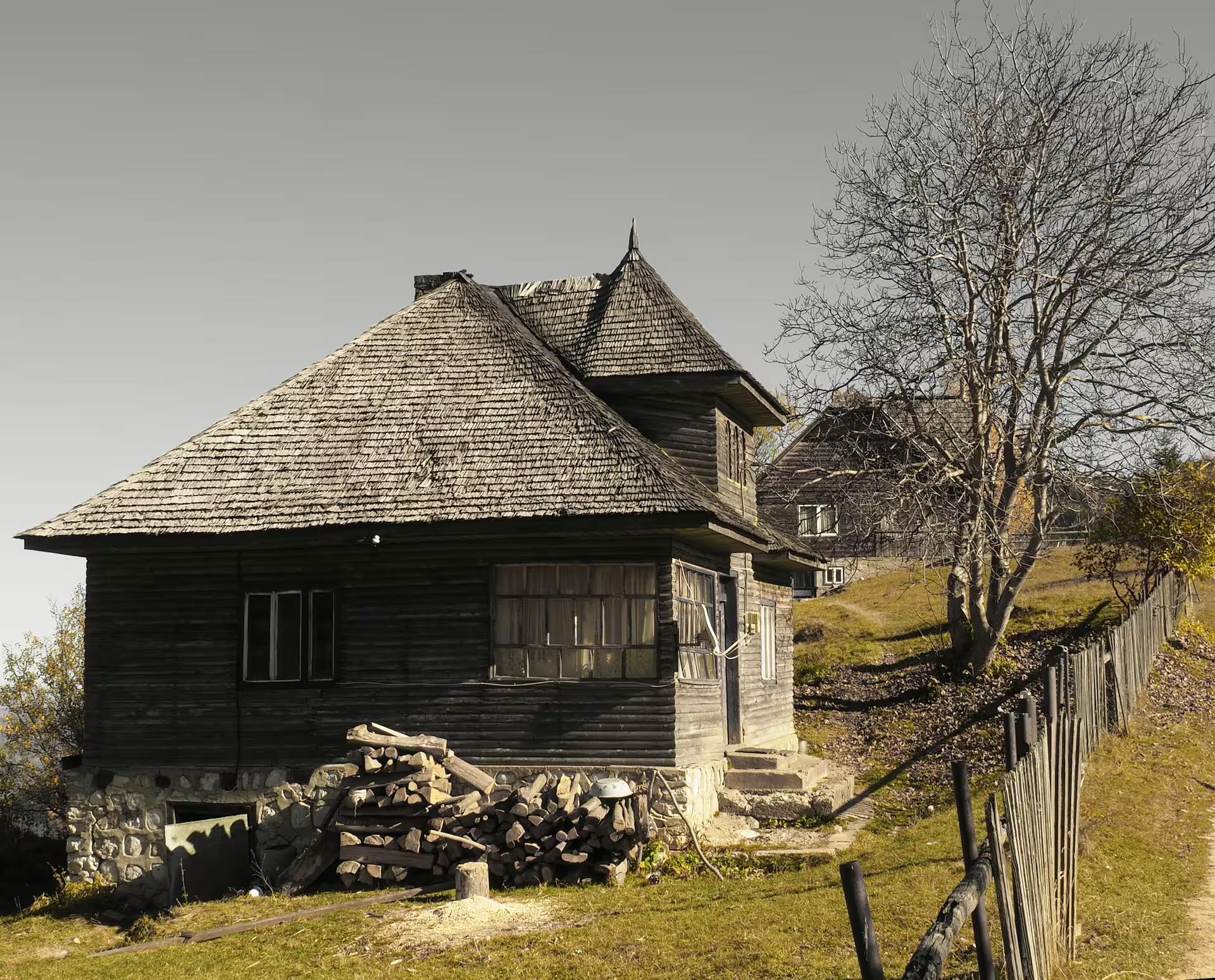 Traditional dark wooden mountain village house with shingled roof and stacked firewood in rural Romania