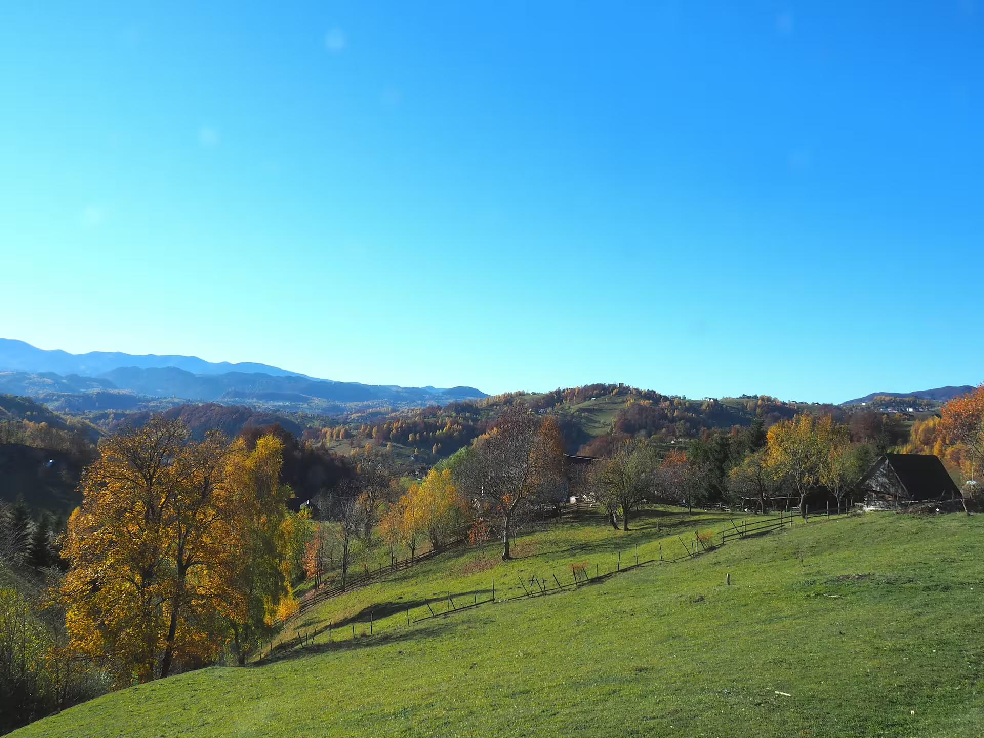 Green hillside meadows with autumn trees and traditional barn overlooking Romanian mountain villages near Brasov