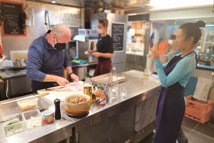 Avignon cooking workshop as exceptional chef prepares seafood while guests watch and film in a market kitchen