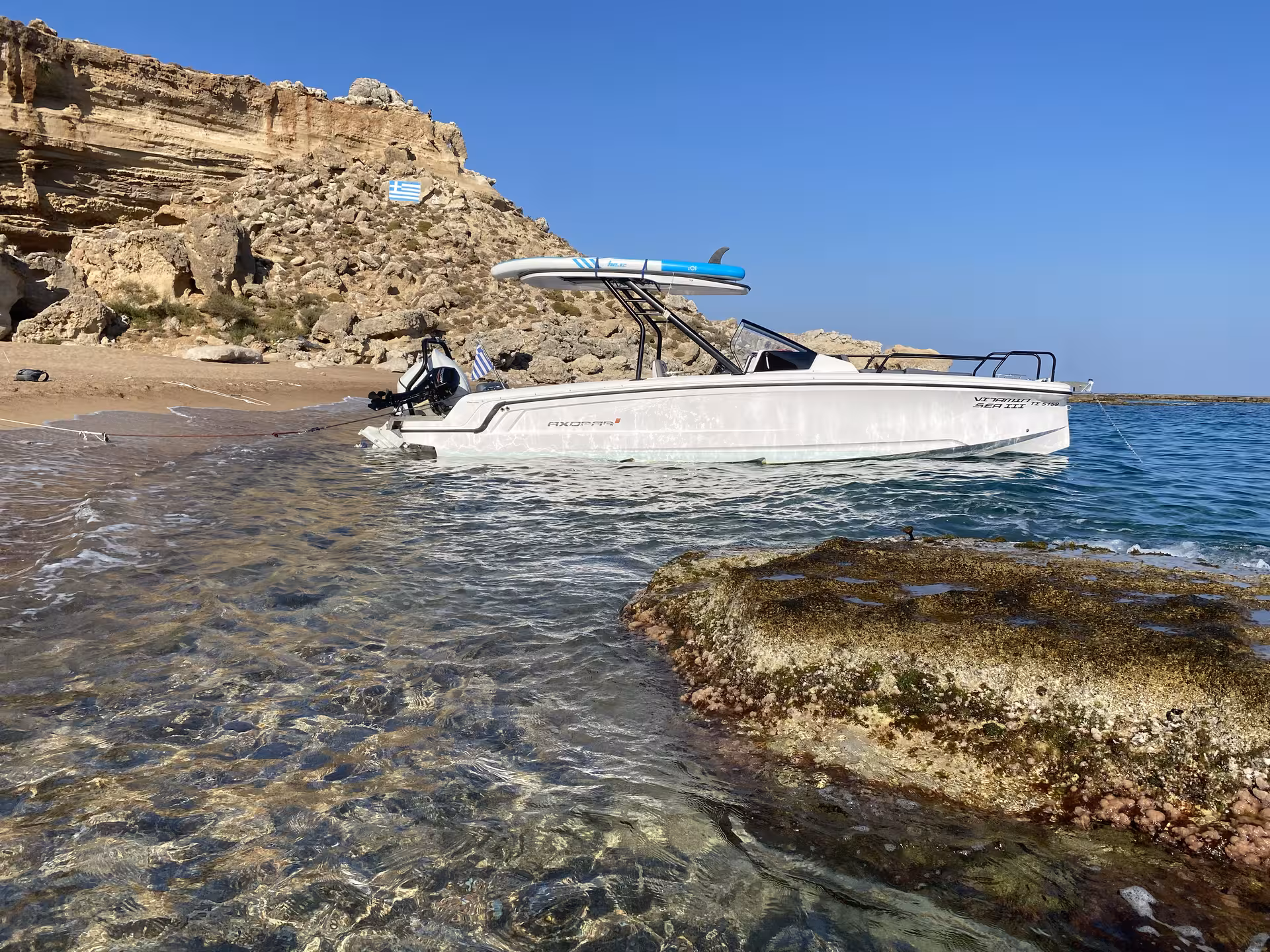 Axopar 25 CT boat rental moored at a secluded beach with crystal-clear water and rugged coastline views