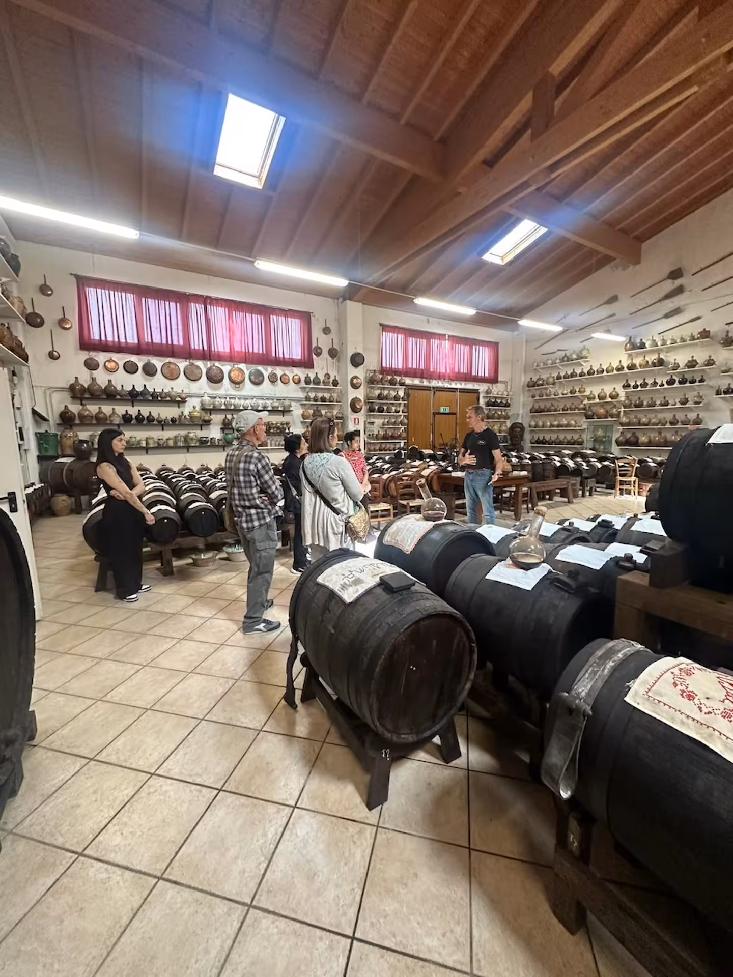 Visitors explore a traditional balsamic vinegar cellar with wooden barrels on a full day tour in Italy.