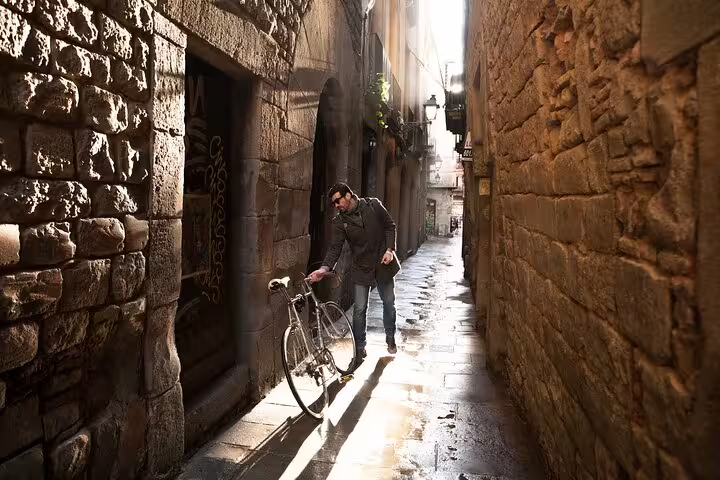 A man with a bicycle explores a narrow, sunlit alley in Barcelona's historic Jewish Quarter during a private religious tour.