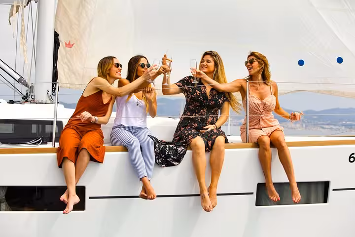 Friends clinking drinks on a Barcelona private sailing tour with open bar and snacks on a small yacht