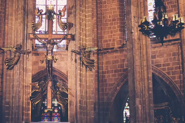 Interior of a Barcelona cathedral featuring a detailed crucifix and ornate stained glass windows.