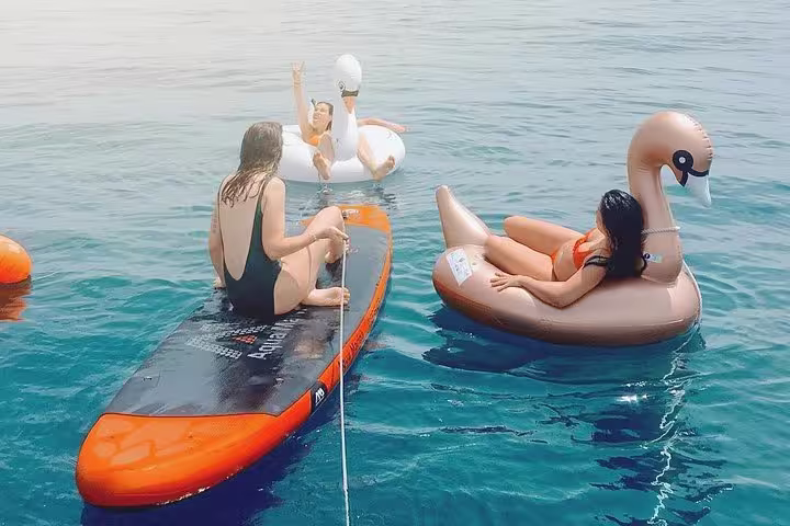 People enjoying a sunny day on inflatable swans and paddleboards during a Barcelona small group sailing tour with cava.