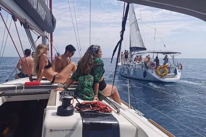 People enjoying a sunny day on a sailing tour near Barcelona, relaxing with snacks and cava on a small group sailboat.