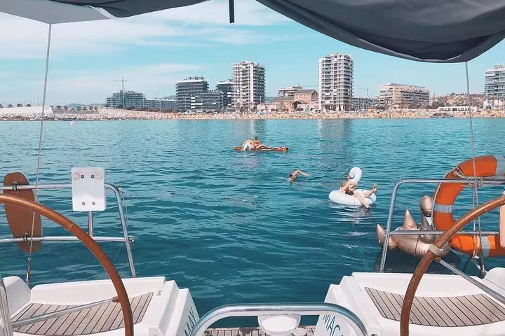 View from a sailboat deck overlooking Barcelona's coastline, with people relaxing in the water, ideal for a small group sailing tour.