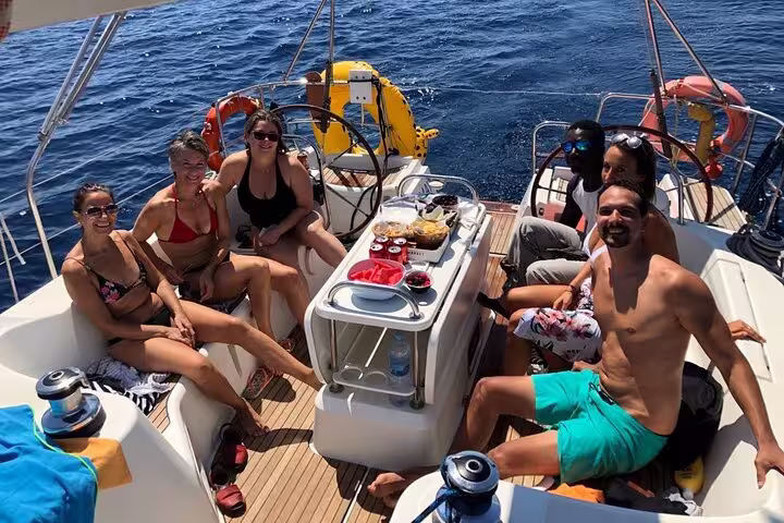 Group enjoying a sunny Barcelona sailing tour with snacks and cava, relaxing on deck with scenic views of the Mediterranean Sea.