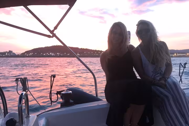 Friends relax on a boat during Barcelona sunset tour with open bar and snacks, skyline glowing pink
