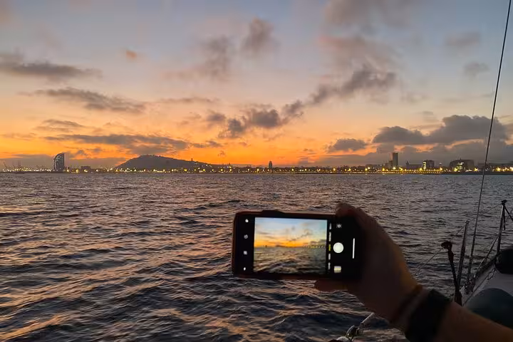 Guest photographing Barcelona sunset from a sailboat, enjoying open bar and snacks on a scenic cruise