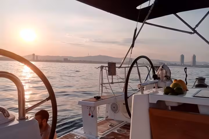 Sailboat deck at sunset off Barcelona with open bar snacks and skyline views on a sailing tour
