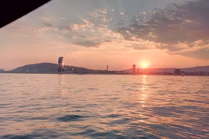 Barcelona coastline sunset from the sea on a sailing tour with open bar and snacks, golden sky reflections