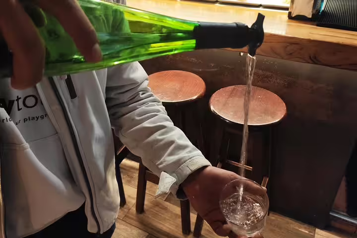 A person pours traditional Spanish cider from a green bottle in a cozy Barcelona tapas bar.
