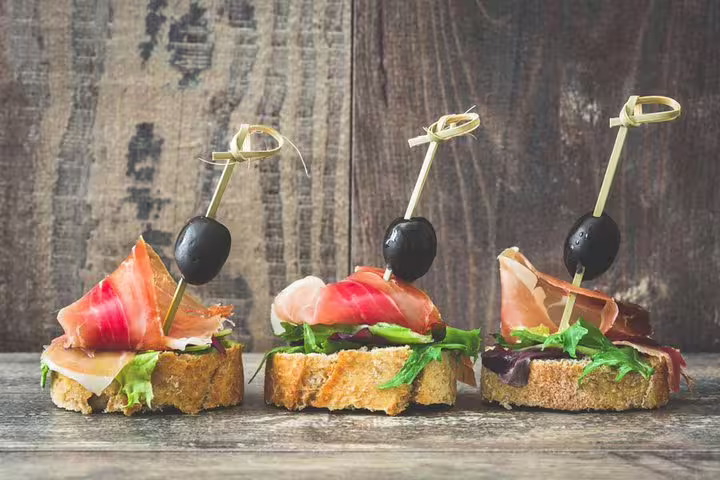 Delicious Spanish tapas with cured ham, olives, and greens on crunchy bread, perfect for a Barcelona tapas and wine tour.