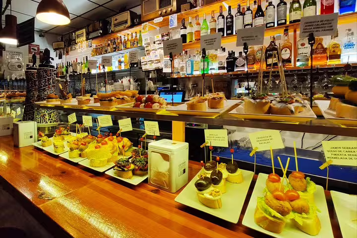 Vibrant display of assorted tapas and wine bottles on a bar counter in a bustling Barcelona neighborhood.