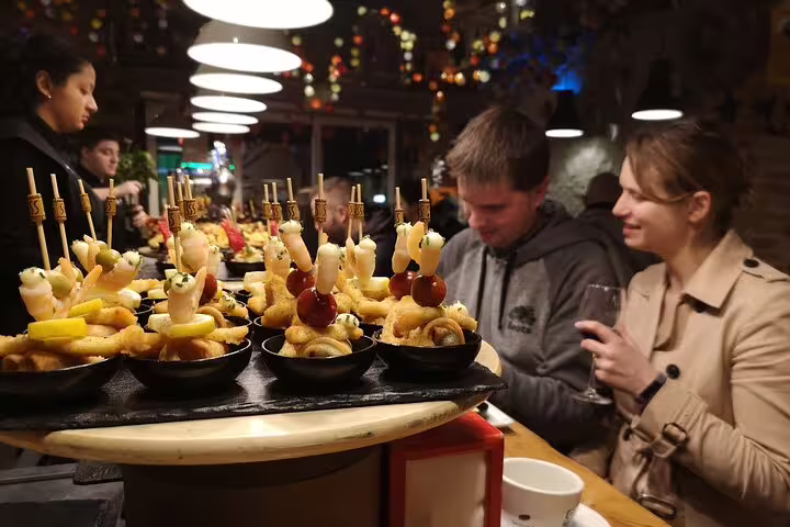 Couple enjoying a Barcelona tapas and wine tour in a traditional tavern, surrounded by delicious pintxos and vibrant atmosphere.